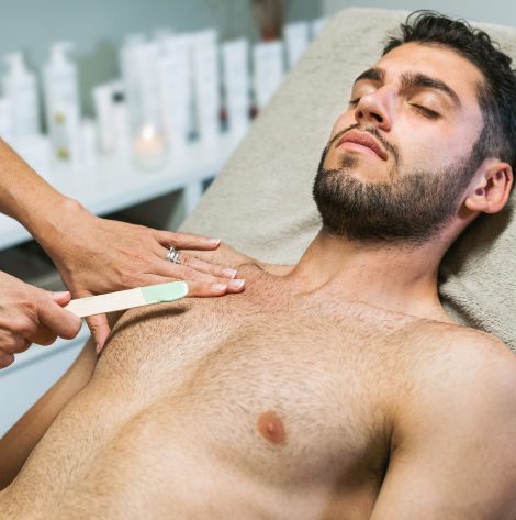 Serene guy getting wax hair removal from chest in salon